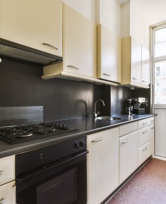 Fragment of interior of light narrow home kitchen with minimalist style white furniture with sink and stove